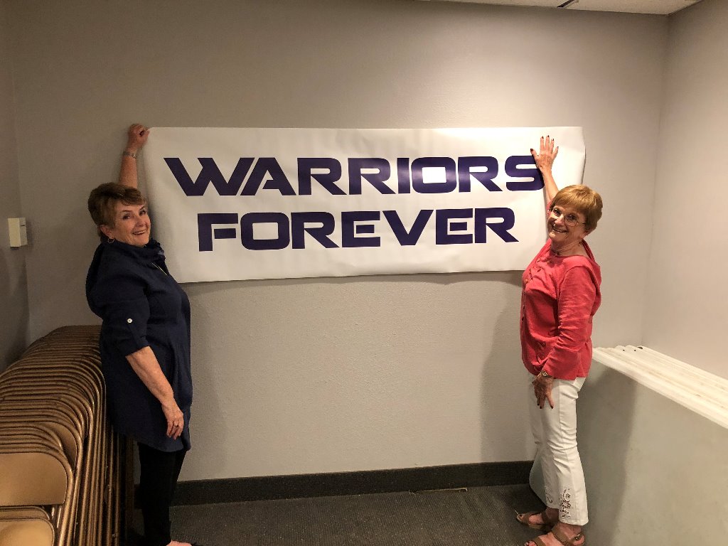 Ruth Illies Licht and Connie Johnson Toavs hanging Warrior Banner